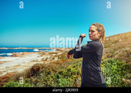 Lo stretching è essenziale per un ottimo allenamento. Una giovane donna sportiva che si stretching prima del suo allenamento all'aperto. Foto Stock