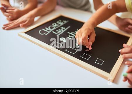 Prendere nota delle loro faccende per il giorno. Primo piano dei bambini che scrivono una lista di faccende su una lavagna a casa. Foto Stock