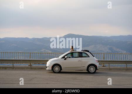 Donna viaggiatore gode di paesaggi rocciosi sopra le nuvole in alta montagna da una piccola auto convertibile. Foto Stock