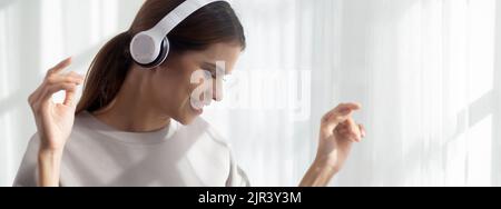 Felice giovane donna asiatica indossando cuffie ascoltare musica mentre balla e cantare con divertimento e godere nel soggiorno, felicità femmina con ente Foto Stock