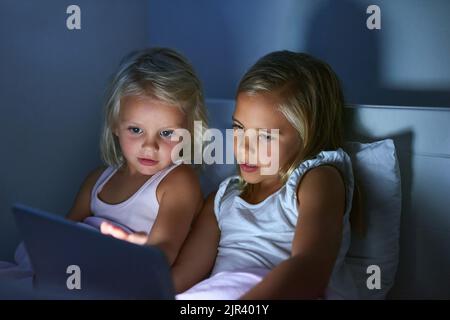 Giocare con le loro app preferite. Due bambine usano un tablet digitale prima di andare a dormire. Foto Stock