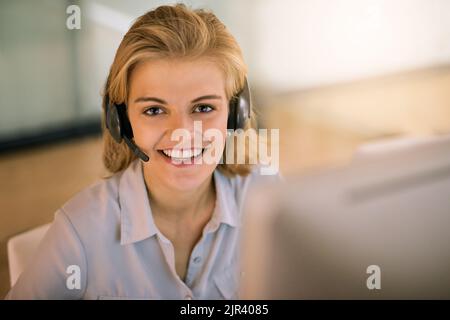Come posso aiutarla oggi. Ritratto ad angolo alto di una giovane donna attraente che lavora in un call center. Foto Stock