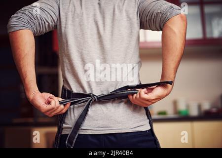 Lascia andare a cucinare. Il retroverview ha sparato un giovane uomo non identificabile legando il grembiule dietro la schiena nella sua cucina a casa. Foto Stock