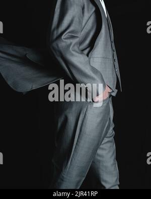 Uomo in tuta grigia su sfondo nero. Uomo d'affari con giacca e pantaloni a piedi. Foto di alta qualità Foto Stock