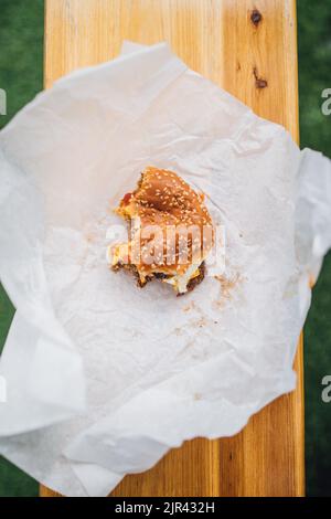 cheeseburger mangiato a metà con panino di sesamo su carta bianca Foto Stock