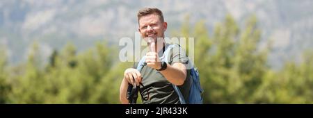 L'uomo con bastoni finlandesi per il nordic walking tiene i pollici in cima alla montagna Foto Stock