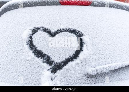 Cuore di neve sul finestrino dell'auto con spazio per la copia. Cuore segno in fiocchi di neve freschi. Simbolo di forma del cuore disegnato sul vetro innevato dell'automobile. Concetto di amore. San Valentino Foto Stock