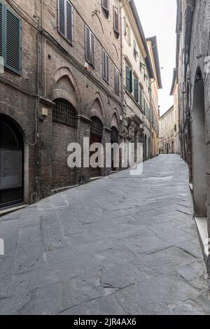 Paesaggio urbano con strada in salita tra vecchi edifici, girato in luce estiva a Siena, Toscana, Italia Foto Stock