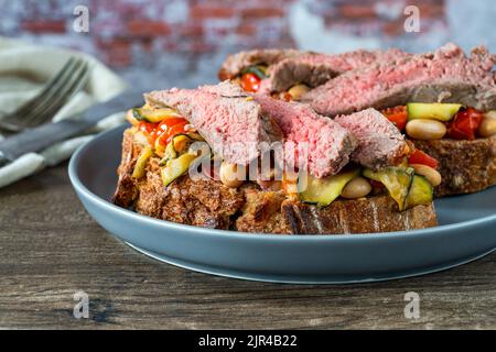 Bistecca di manzo su pasta madre con pomodori ciliegini, zucchine e fagioli cannellini Foto Stock