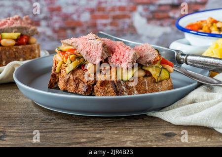 Bistecca di manzo su pasta madre con pomodori ciliegini, zucchine e fagioli cannellini Foto Stock