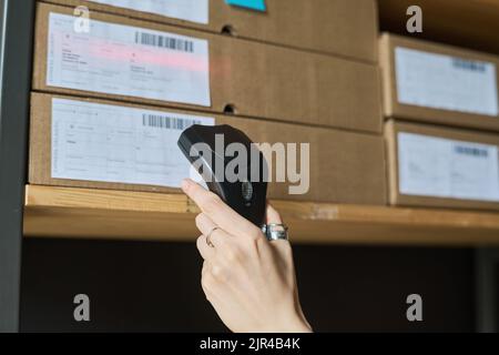 Primo piano di una donna che esegue la scansione di codici a barre su pacchi con scanner mentre lavora in magazzino Foto Stock