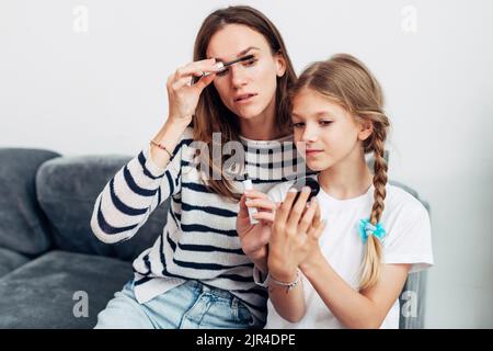 Donna applica mascara alle sue ciglia sua figlia sta tenendo uno specchio. Foto Stock