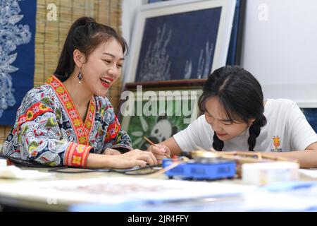 (220822) -- GUIYANG, 22 agosto 2022 (Xinhua) -- Zhang Juanjuan (L) istruisce sua sorella a fare una pittura batik in uno studio batik DIY ad Anshun, nella provincia di Guizhou del sud-ovest della Cina, 18 agosto 2022. Zhang Juanjuan, una ragazza del gruppo etnico di Miao, ha deciso di tornare a casa per prendere il controllo dei suoi genitori affari relativi ai prodotti batik fare dopo la laurea. Batik è un patrimonio culturale immateriale nella sua città natale. Ha registrato il laboratorio di batik dei suoi genitori come una società d'arte batik, e ha fondato il suo studio batik DIY. Per espandere la propria attività, Zhang Juanjuan e i suoi colleghi hanno progettato pratiche, Foto Stock