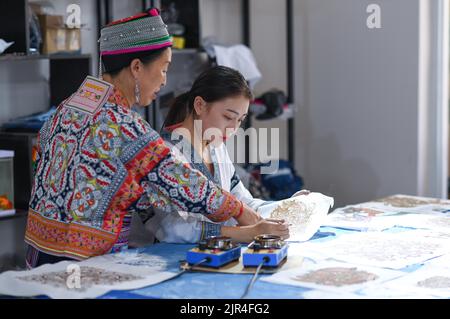 (220822) -- GUIYANG, 22 agosto 2022 (Xinhua) -- Zhang Juanjuan (R) parla con sua madre sulle tecniche di realizzazione di dipinti batik in uno studio batik ad Anshun, nella provincia di Guizhou, nel sud-ovest della Cina, il 18 agosto 2022. Zhang Juanjuan, una ragazza del gruppo etnico di Miao, ha deciso di tornare a casa per prendere il controllo dei suoi genitori affari relativi ai prodotti batik fare dopo la laurea. Batik è un patrimonio culturale immateriale nella sua città natale. Ha registrato il laboratorio di batik dei suoi genitori come una società d'arte batik, e ha fondato il suo studio batik DIY. Per espandere la propria attività, Zhang Juanjuan e i suoi colleghi hanno des Foto Stock