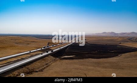 Autostrada che attraversa un terreno agricolo bruciato dal sole Foto Stock