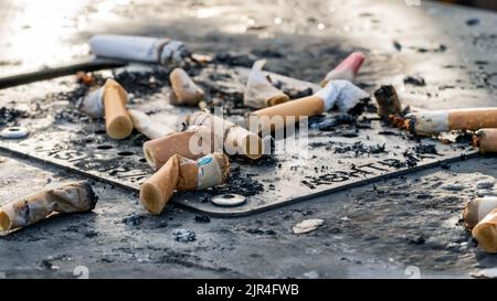 I mozziconi di sigaretta usati gettati sulla superficie sporca del posacenere Foto Stock