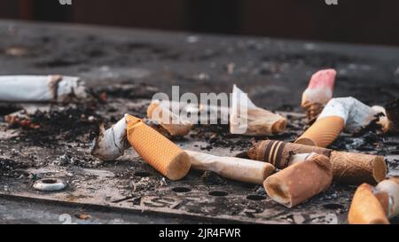 I mozziconi di sigaretta usati gettati sulla superficie sporca del posacenere Foto Stock