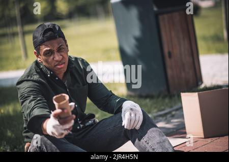 Uomo seduto a terra che tiene la mano alla fotocamera Foto Stock
