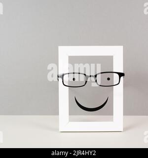 Telaio con un volto felice con occhiali, concetto di salute mentale, mentalità ed emozione positiva, sostegno e simbolo di valutazione Foto Stock