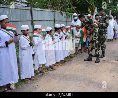 I funzionari della BSF (Border Security Force) distribuiscono la bandiera indiana ai bambini per partecipare a una "Tiranga Yatra" organizzata dalla BSF (Border Security Force) nell'ambito delle celebrazioni "Azadi ka Amrit Mahotsav" per commemorare il 75th° anniversario della giornata dell'indipendenza dell'India lungo la recinzione di confine India-Bangladesh nella zona di Boxanagar. Agartala. Tripura, India. Foto Stock