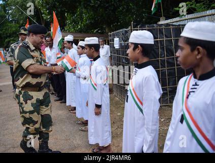 I funzionari della BSF (Border Security Force) distribuiscono la bandiera indiana ai bambini per partecipare a una "Tiranga Yatra" organizzata dalla BSF (Border Security Force) nell'ambito delle celebrazioni "Azadi ka Amrit Mahotsav" per commemorare il 75th° anniversario della giornata dell'indipendenza dell'India lungo la recinzione di confine India-Bangladesh nella zona di Boxanagar. Agartala. Tripura, India. Foto Stock