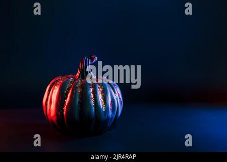 Zucca decorativa con scintille arancioni in rosso neon e luce blu al buio. Arredamento e sfondo di Halloween con spazio copia. Messa a fuoco selettiva. Foto Stock