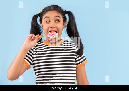 Primo piano di bambina lollipop leccando su sfondo semplice Foto Stock