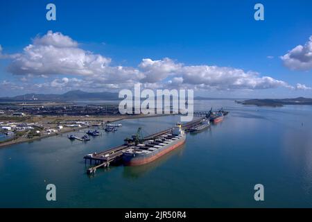 Vista aerea delle navi da carico attraccate in un trafficato porto industriale con cieli limpidi e acque blu calme. Gladstone, Queensland, Australia Foto Stock