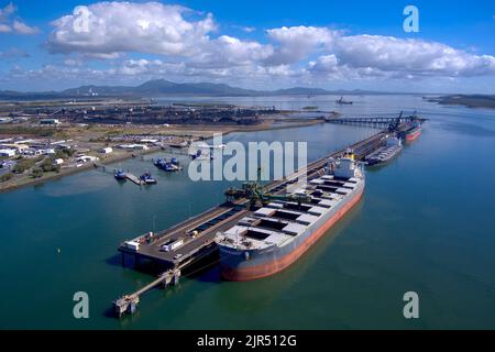Vista aerea delle navi da carico attraccate in un trafficato porto industriale con cieli limpidi e acque blu calme. Gladstone, Queensland, Australia Foto Stock