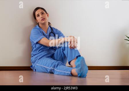 Stanca giovane infermiera seduta sul pavimento di un corridoio ospedaliero Foto Stock