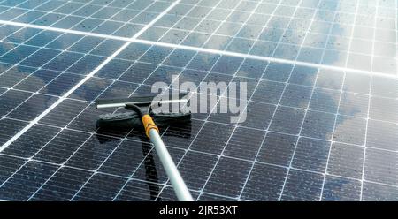 Pulizia pannello solare con mop in microfibra su tetto bagnato. Servizio di manutenzione di pannelli solari o moduli fotovoltaici. Risorsa sostenibile. Energia solare. Verde Foto Stock