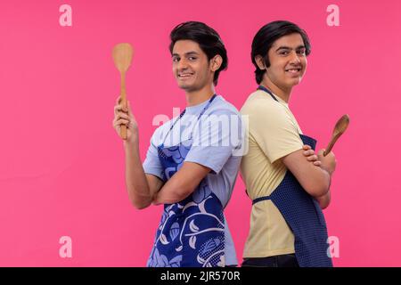 Due ragazzi adolescenti in grembiule chef in piedi con spatole su sfondo rosa Foto Stock