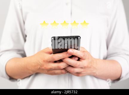 Mani che tengono il telefono per dare un buon feedback. Donna che presenta una valutazione a cinque stelle. Sondaggio sulla soddisfazione dei consumatori. Parere positivo. Merci, servizi, hotel, valutazione delle applicazioni. Foto di alta qualità Foto Stock