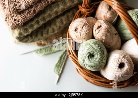 Fili di filo verde e marrone in un cesto per maglieria di abiti caldi con aghi per maglieria e prodotti finiti in filo, hobby per maglieria Foto Stock