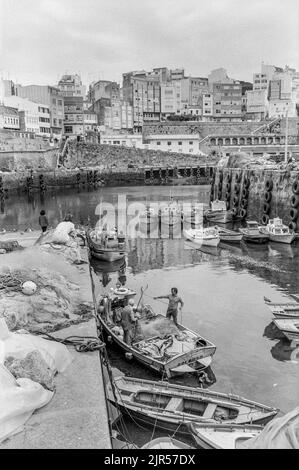 SPAGNA - Galizia - 1970s. Pescatori che preparano le loro barche nel porto di Malpica con la città sullo sfondo., Galizia, Spagna nordoccidentale. Copyright Pho Foto Stock