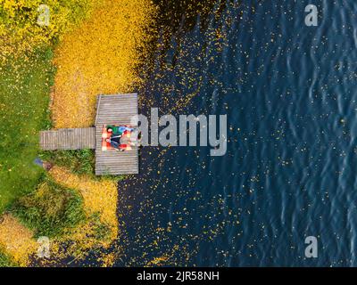 coppia posata sul molo al lago coperto di foglie autunnali Foto Stock