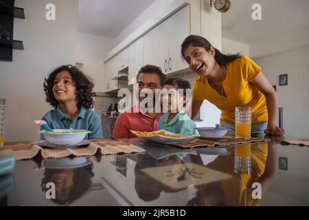 Ritratto di una felice famiglia nucleare che guarda via durante la colazione Foto Stock