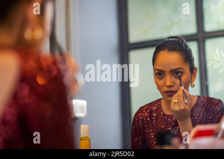 Giovane donna che applica eyeliner di fronte allo specchio Foto Stock