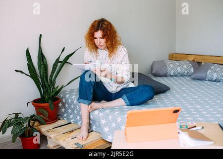 Donna adulta attraente che studia da casa su corsi online utilizzando il tablet Foto Stock