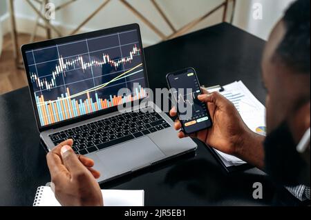 Primo piano di cripto trader investitore broker utilizzando cellulare e computer portatile per l'analisi del mercato finanziario criptovaluta, l'acquisto o la vendita di criptovaluta, i diagrammi azionari sono su computer portatile e cellulare schermo Foto Stock