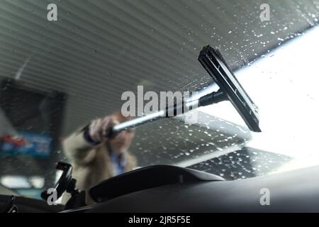 Primo piano di un uomo d'affari senior lavando la finestra dell'auto alla stazione di servizio. Foto Stock