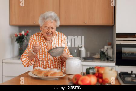 Buona donna anziana zuccherare il pane dolce intrecciato fatto in casa con uva passa. Foto Stock