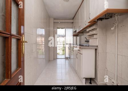 Cucina con armadi in legno bianco lucido, piani in pietra grigia, elettrodomestici in acciaio inox incorporati, passaggio al piccolo ponte e pavimenti piastrellati Foto Stock