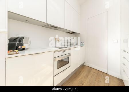 Cucina con armadi in legno bianco lucido, ripiani in pietra bianca, elettrodomestici bianchi da incasso e pavimenti in legno di castagno Foto Stock