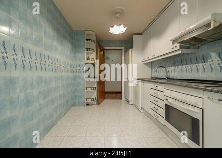 Grande cucina con armadietti di legno bianco lucido, ripiani in pietra di granito, elettrodomestici bianchi da incasso, e brutto blu e pavimenti in piastrelle bianche Foto Stock