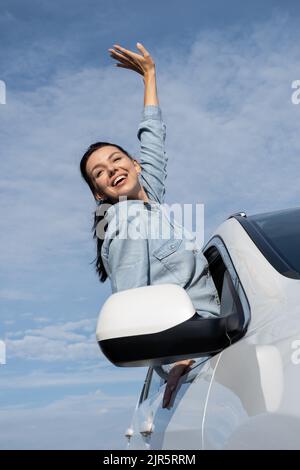 Donna felice che si inclina fuori dal finestrino dell'auto. Giovane donna turistica in auto sulla porta d'ingresso, guarda la strada. Foto Stock