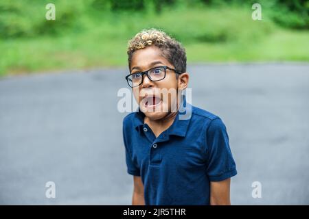 Un ragazzo di età elementare afro-americana che indossa occhiali in piedi fa una faccia scioccata e spaventata sciocca Foto Stock