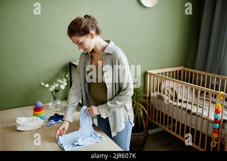 Giovane donna incinta che prepara le cose per il suo bambino in piedi nella stanza del bambino Foto Stock