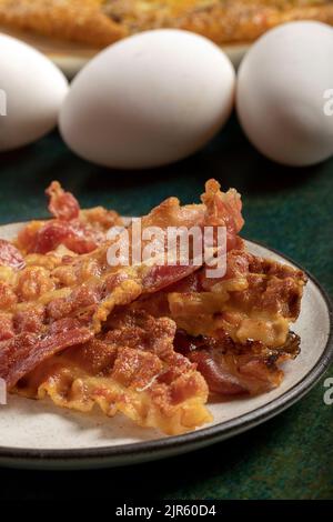 Primo piano di alcune fette croccanti di pancetta e tre uova fresche sullo sfondo. Foto Stock