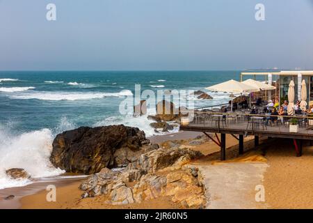 Onde che si schiantano su una spiaggia vicino a un caffè e bar sulla costa atlantica a Foz do Douro vicino a Porto, nel nord del Portogallo. Foto Stock